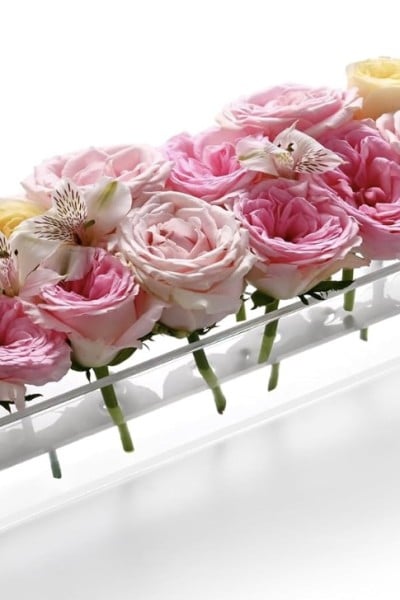 A rectangular glass vase holds a row of pink and white roses, with a few white lilies interspersed. The flowers are arranged neatly, creating a harmonious and elegant Valentine's table centerpiece.